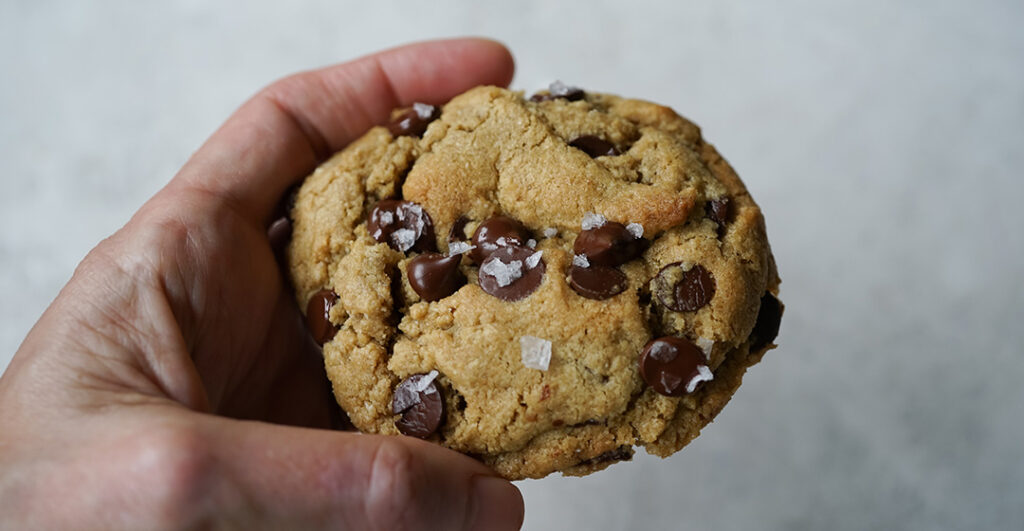 A Gluten-Free Chocolate Chip Cookie held in hand