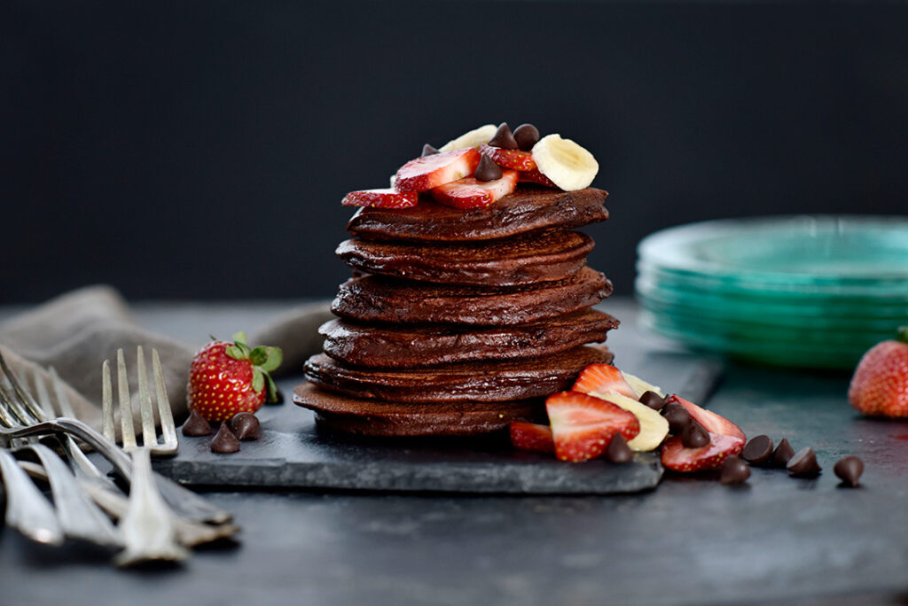 Gluten-Free Chocolate Banana Pancakes in a stack with strawberries and bananas