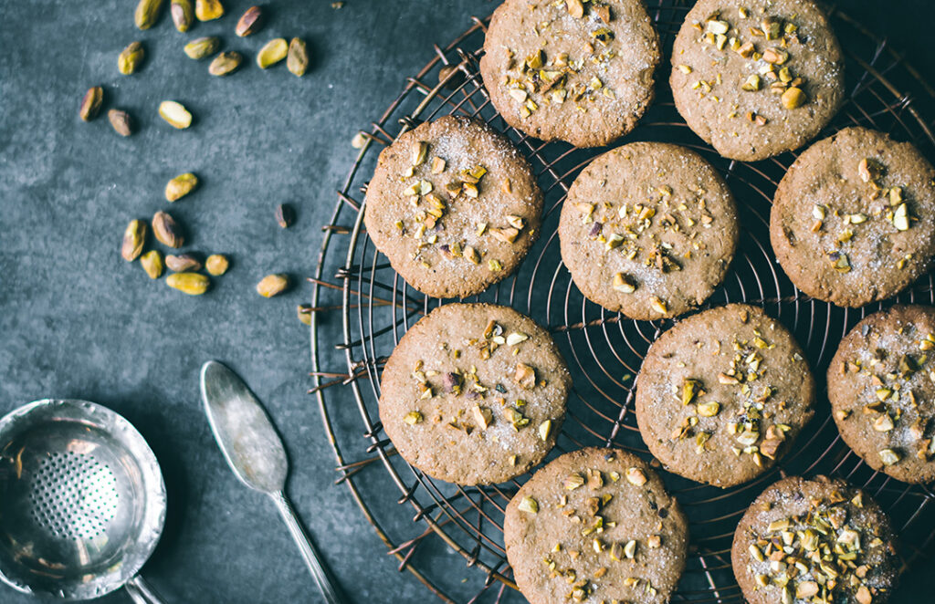 Teff Pistachio Biscuits displayed on cooling tray with pistachios strewn about