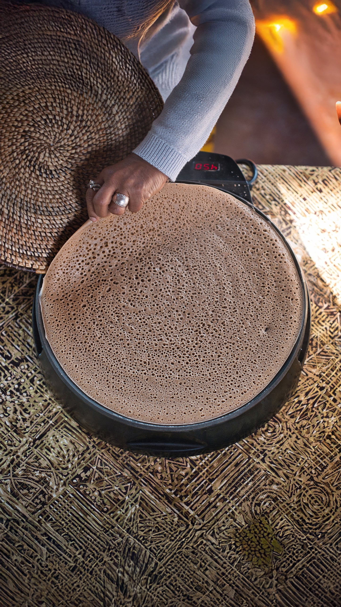 Person holding a woven basket over a hot stone grill with injera on it.