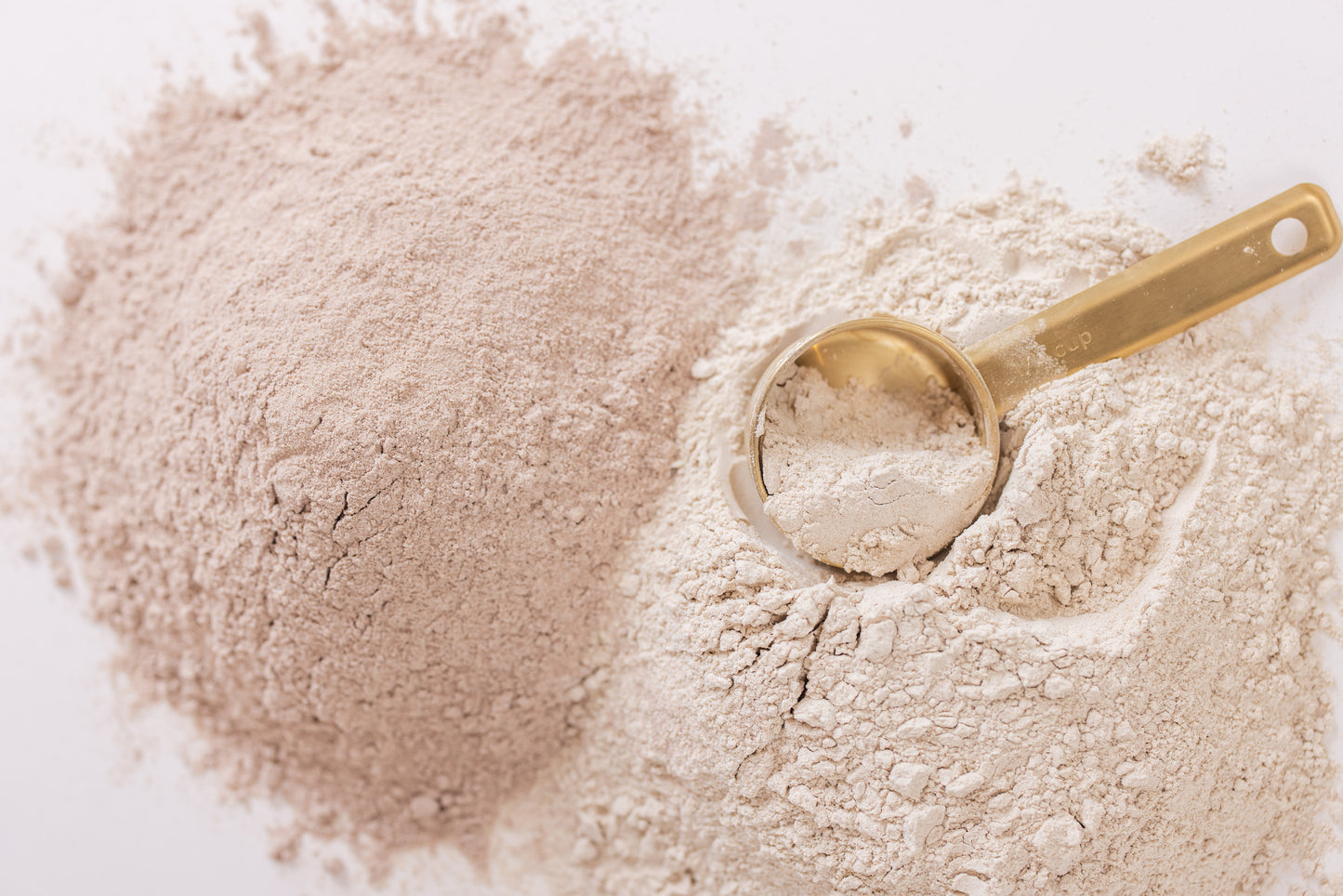 Gold measuring spoon in a pile of flour on a white background