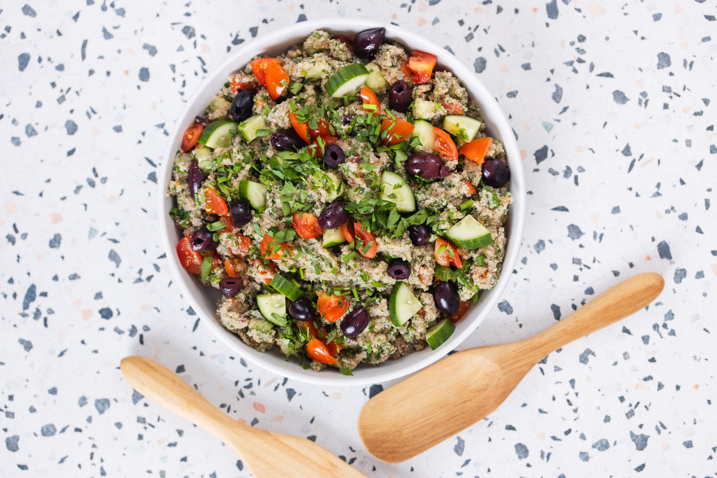 Vegetable salad with teff in a white bowl on a speckled countertop